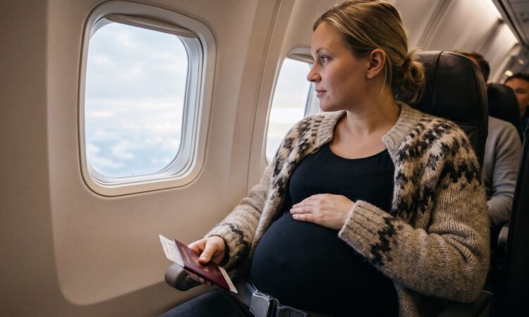 Gravid kvinna sitter på fönsterplats i ett flygplan med säkerhetsbältet spänt lågt under magen