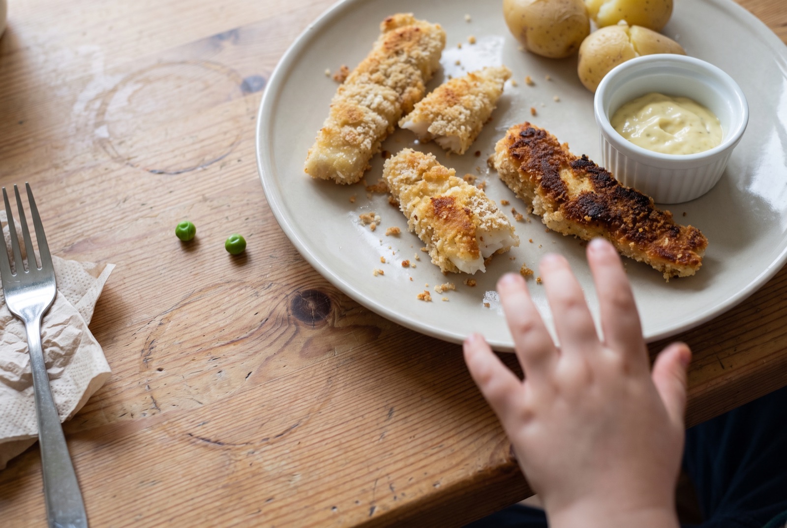 Hemgjorda panerade fiskpinnar av torskrygg på en tallrik med potatis och remoulad