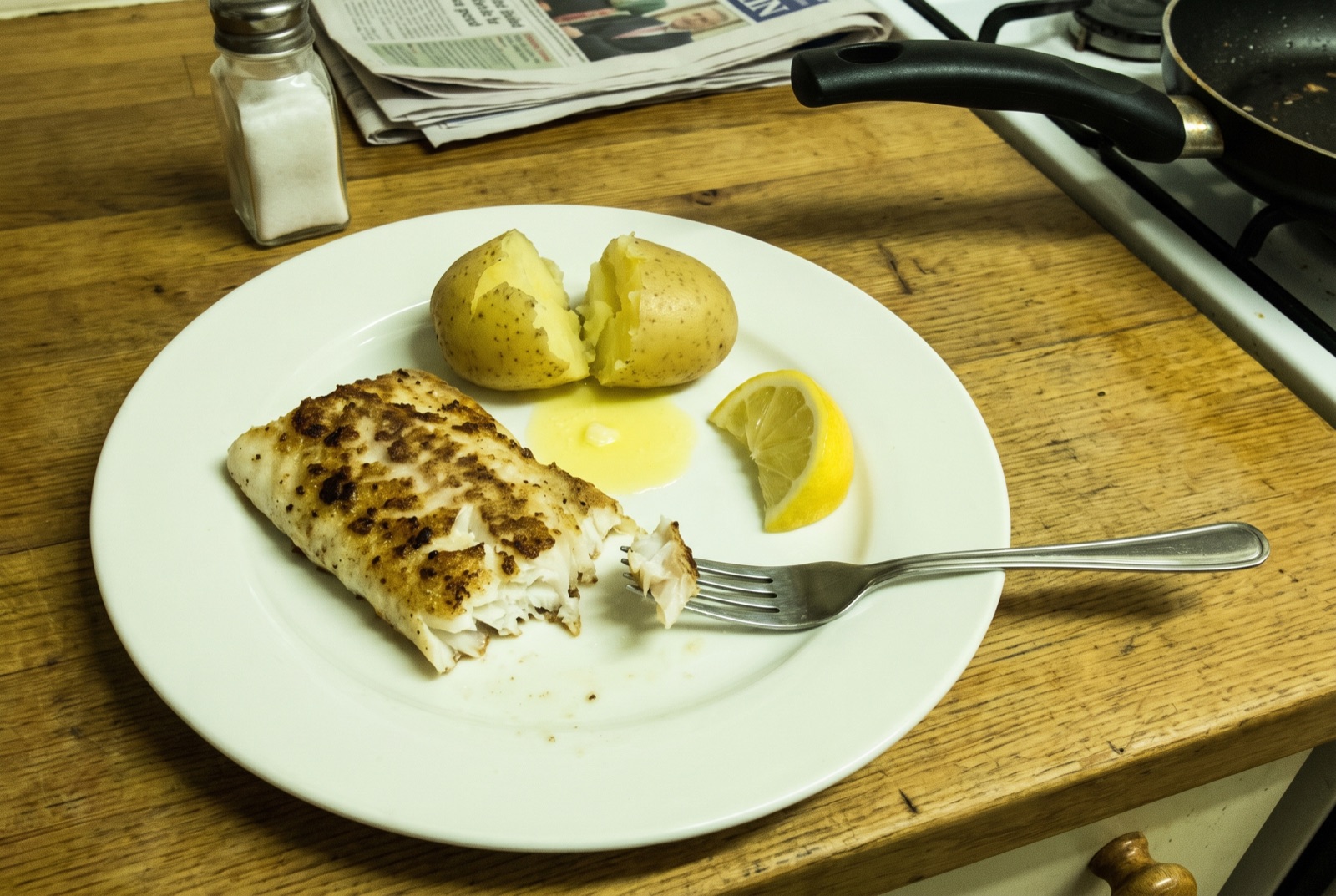 Stekt torskrygg med kokt potatis och citronklyfta på en vanlig tallrik