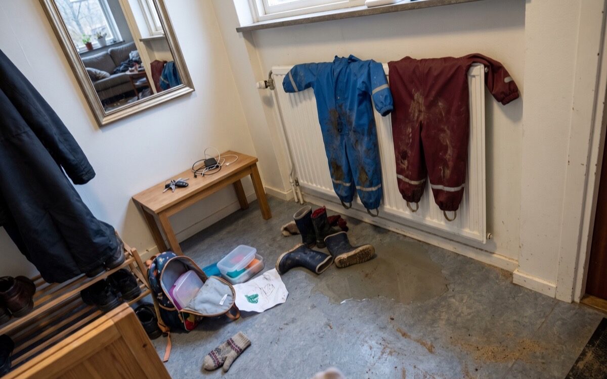 Hall med blöta regnoveraller på elementet, gummistövlar och en öppen ryggsäck på golvet en eftermiddag
