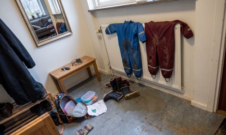 Hall med blöta regnoveraller på elementet, gummistövlar och en öppen ryggsäck på golvet en eftermiddag