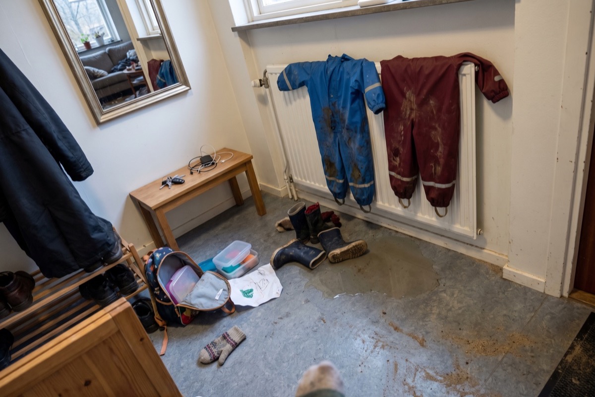 Hall med blöta regnoveraller på elementet, gummistövlar och en öppen ryggsäck på golvet en eftermiddag