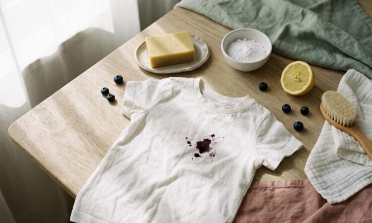 Barn-t-shirt med blabarsflack pa ett kaksbord, bredvid galltval, bikarbonat, citron och borste